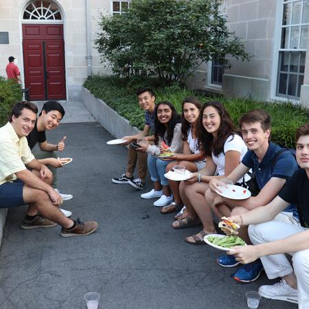students sitting on steps in courtyard with BBQ food