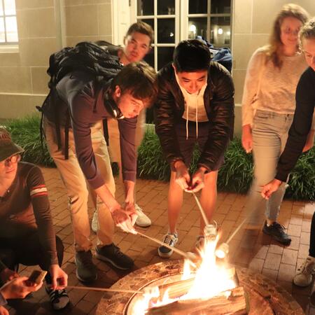 students roasting s'mores around a fire in the courtyard
