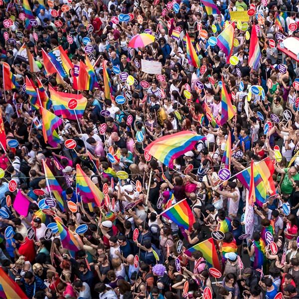 Aerial view of hundreds of people in a crowd waving rainbow flags.