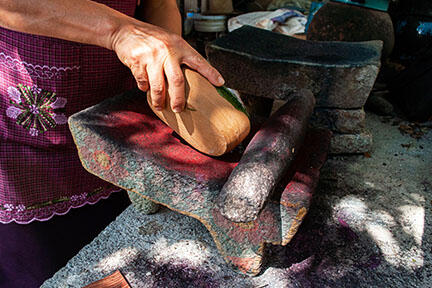 Woman using a flat stone and wood to grind cochineal. 