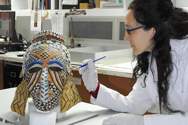conservator works with kuba mask in lab.