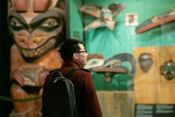 visitor looks at carved pole and masks.