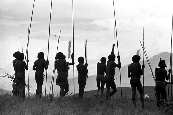 Warriors leaning on their long spears, watching a war in the distance.