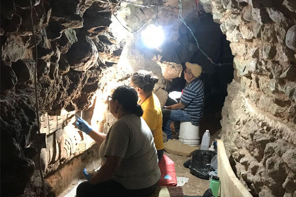 Three people conducting restoration on a stucco facade in a tunnel, Copan, Honduras