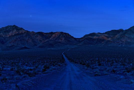 A clear sky above a desert road leading into a mountain range