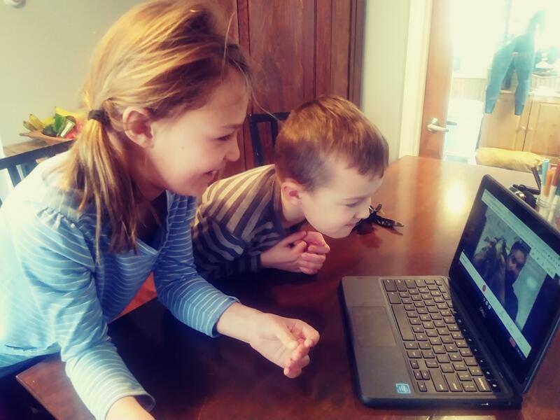 A young boy and girl watching an educator with a frog on a computer screen.