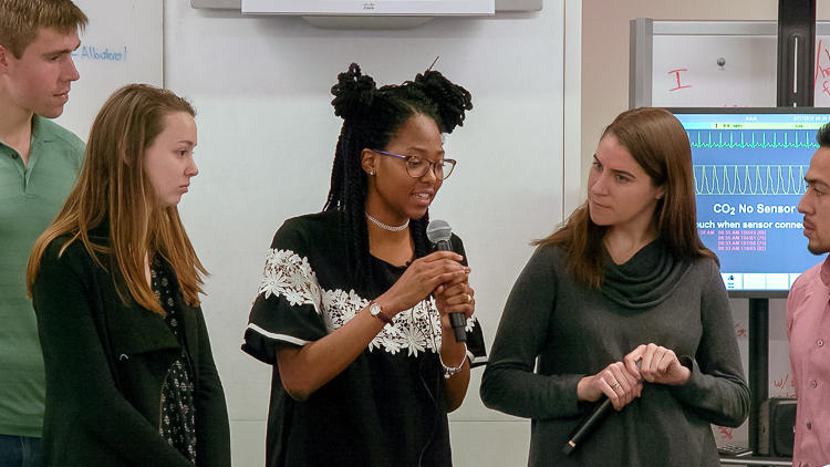 Close up of graduate student speaking with microphone in a group of 4 other students.