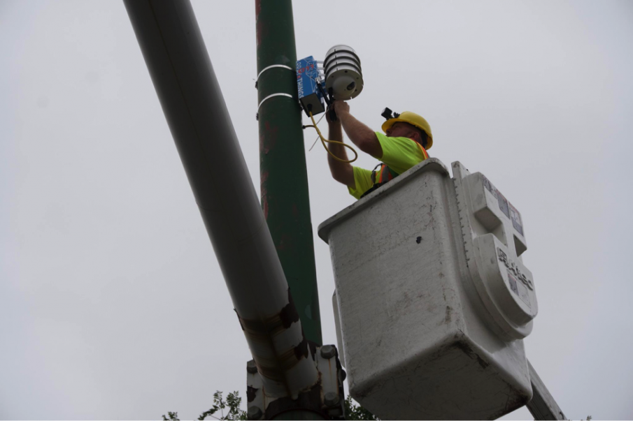 A City of Chicago employee on a ladder installing an AoT node on a lightposta light post