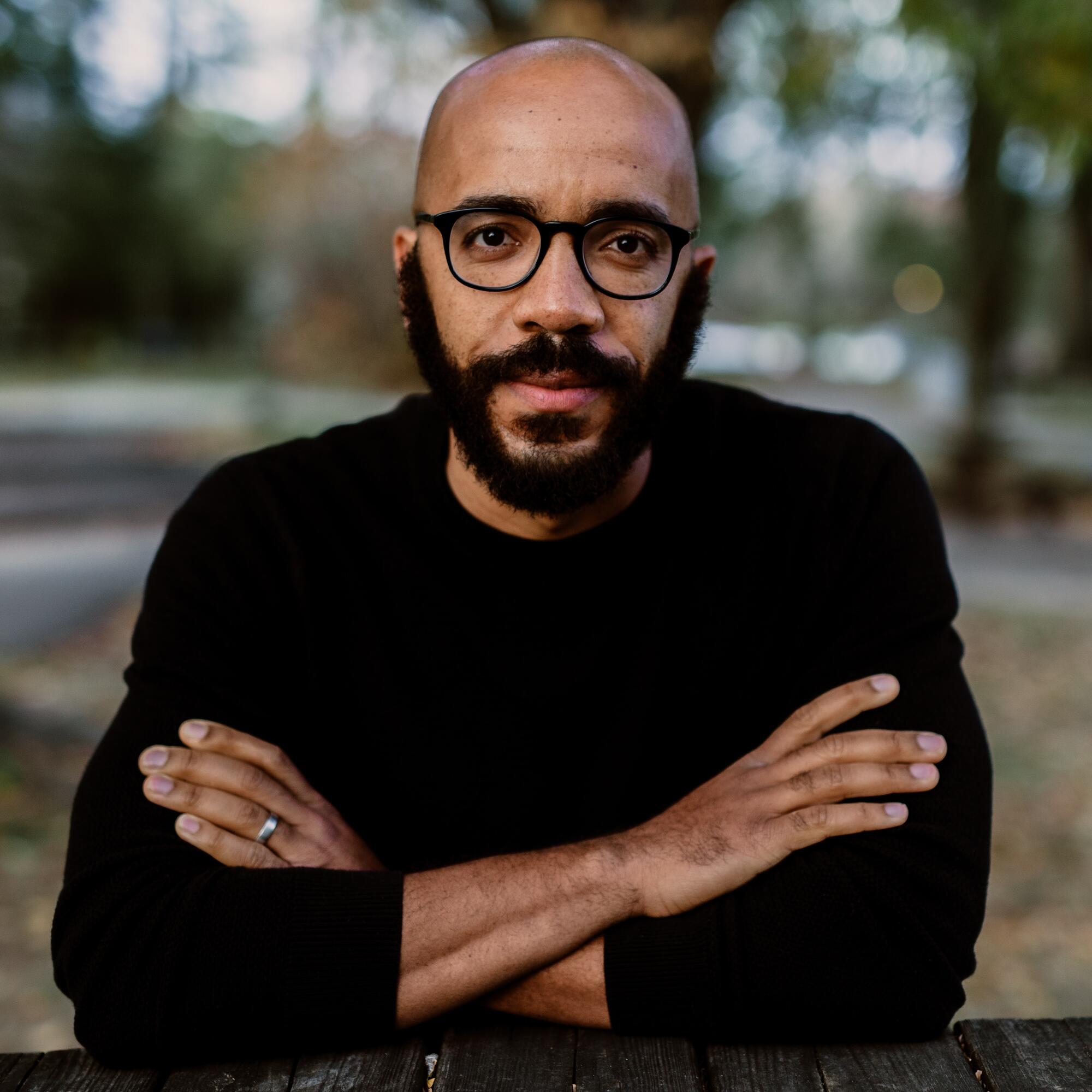 Author Clint Smith in a black sweater, glasses, and full beard
