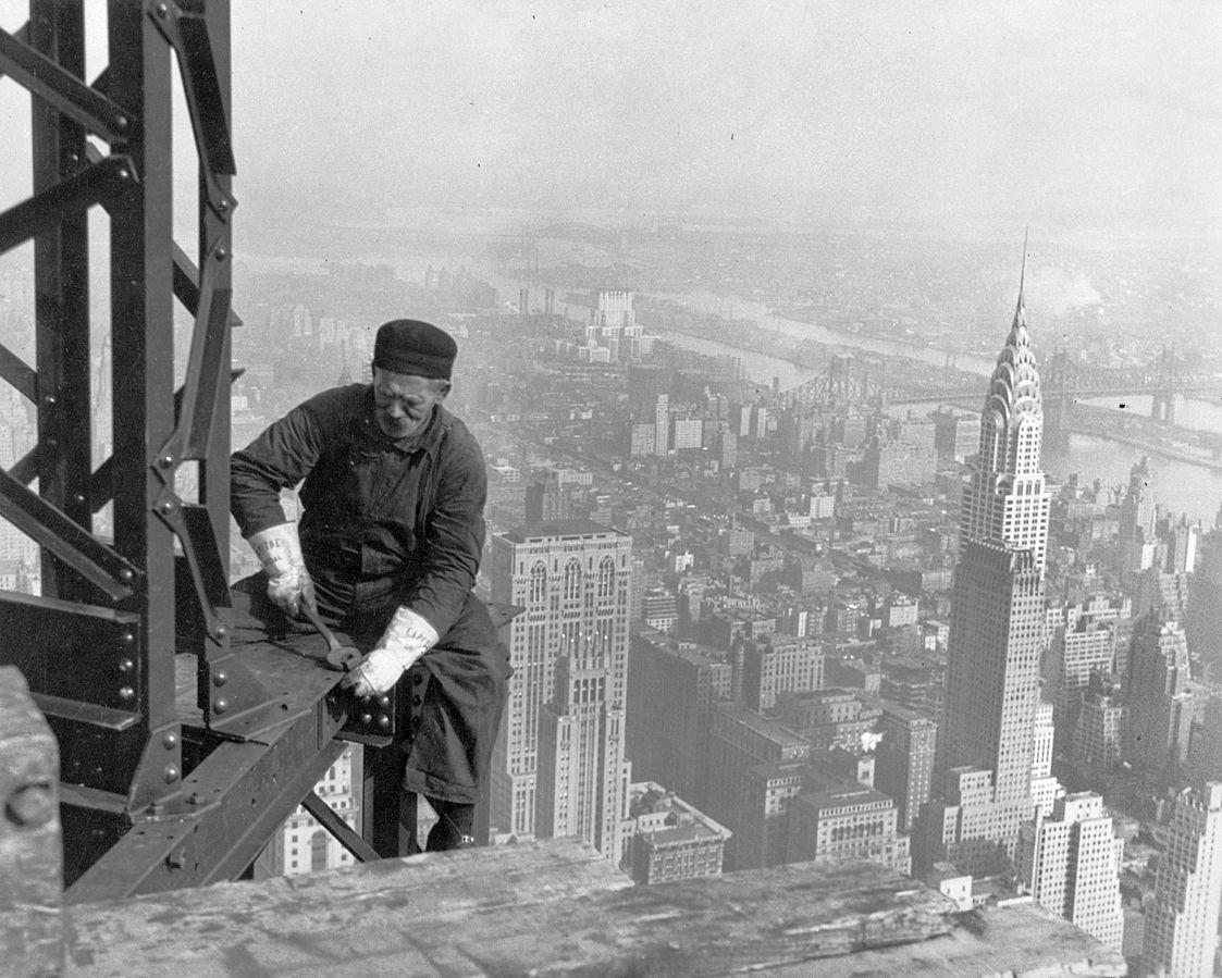Black and white photo of construction worker on scaffolding on high building in NYC.