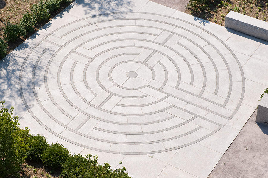 Flat stone circular labyrinth surrounded by shrubbery and a stone bench