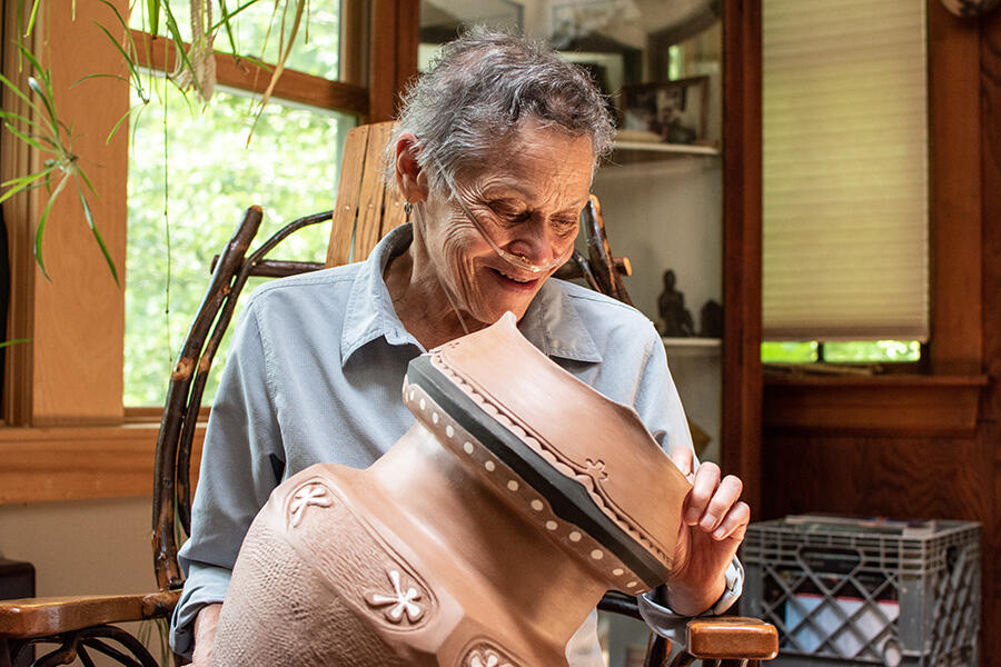 Ramona Peters holding and looking at a brown clay pot with white inlay gliphs
