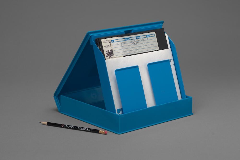 An open plastic case displaying a labeled floppy disks, next to a pencil to show scale.