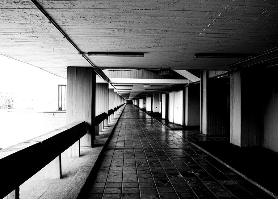 Black and white photo of an indoor/outdoor hallway in 20th century architecture.