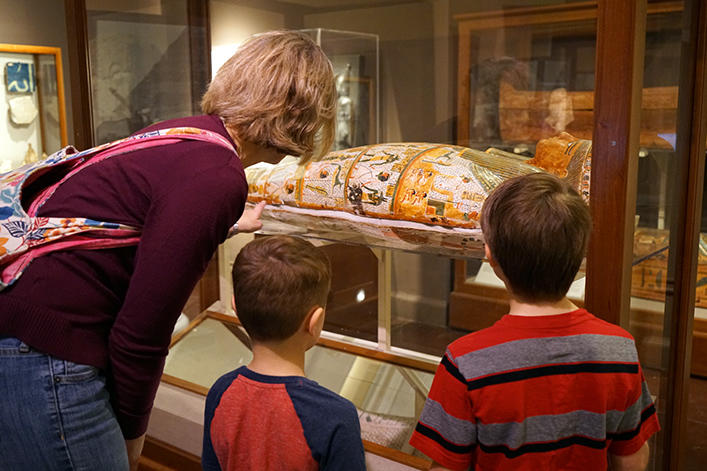 A woman with two kids looking at a mummy.