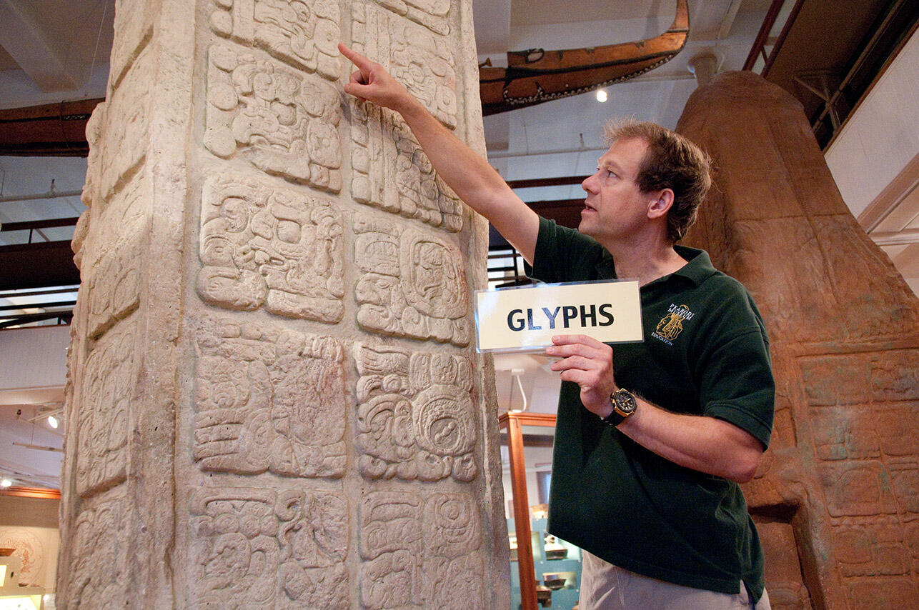 teacher points to life-size maya monument glyph holdng glyph sign.