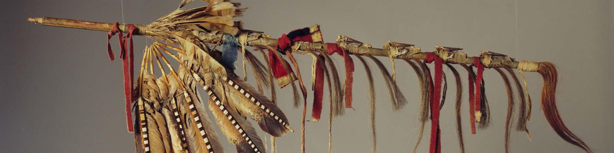 Ceremonial pipe decorated with striped feathers and red and blue ribbon.