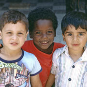 Three children in Akko draw together and smile for the photographer's camera.