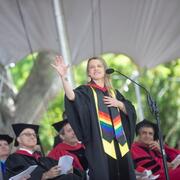 Lindsay Sanwald in black academic regalia holding her right hand up standing in front of seated people during Harvard's Commencement ceremony