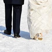 Man in suit and woman in wedding dress walk through snow, with backs to the camera
