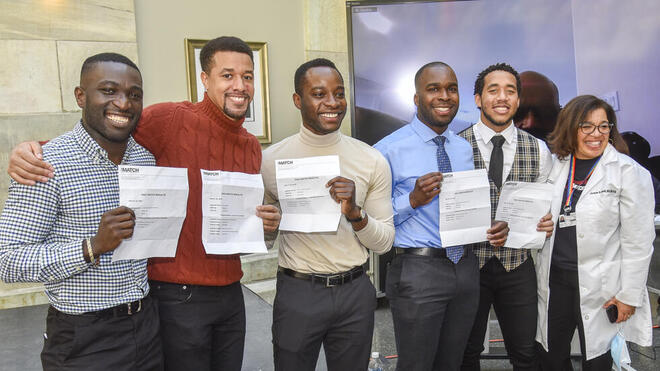 5 medical students stand in a line displaying their Match letters with Dr. Andrea Reid. Image: Steve Lipofsky 